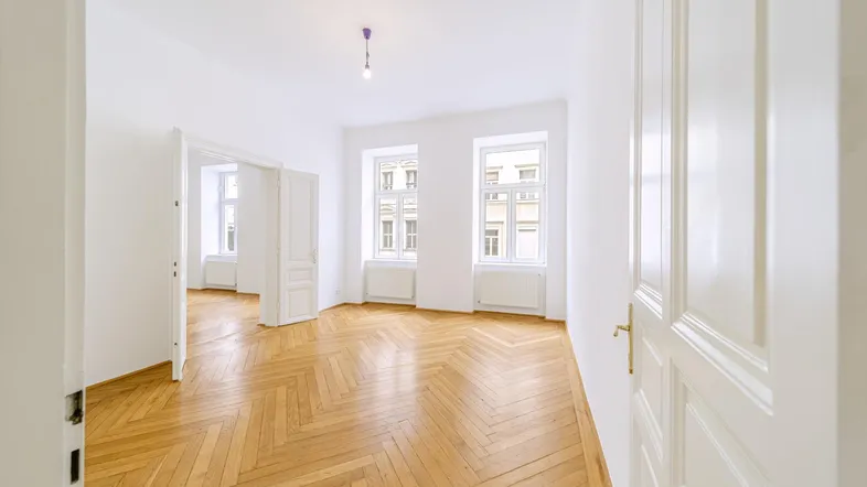 Helles, geräumiges Zimmer mit klassischem Fischgrätparkett und hohen Türen, das viel Tageslicht erhält.