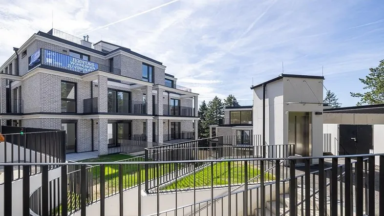 Modernes Apartmentgebäude mit mehreren Etagen, Balkonen und Zugang zur Tiefgarage über eine Rampe.