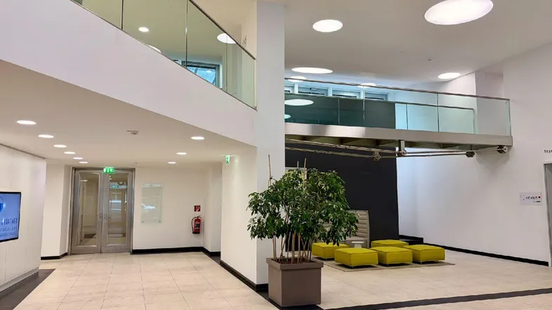 Geräumige, moderne Lobby mit Fliesenboden, einer Galerie und einer Sitzecke mit gelben Hockern.