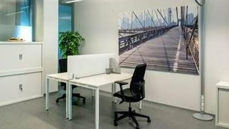 Helles und modernes Büro mit zwei Arbeitsplätzen, weißen Schränken und einem großen Fenster, das viel Tageslicht hereinlässt.