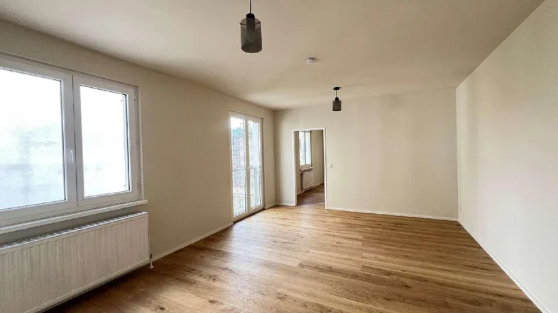 Helles Zimmer mit Holzboden, großen Fenstern und Zugang zu einem Balkon oder einer Terrasse.