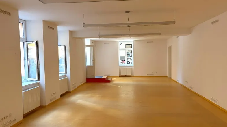 Geräumiger, leerer Gewerberaum mit hellen Wänden, vielen Fenstern und leuchtend gelbem Boden.