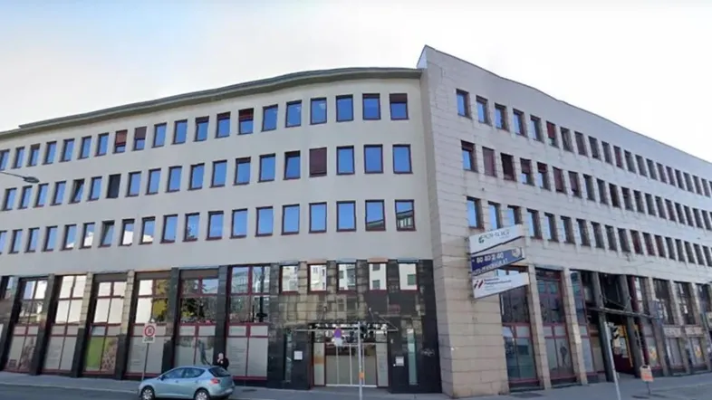 Modernes Bürogebäude mit mehreren Etagen, großen Fenstern im Erdgeschoss und einer hellen Fassade an einer städtischen Straße.