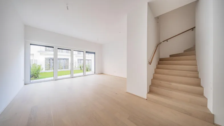 Helles, leeres Wohnzimmer mit Parkettboden, großen Fenstern und Zugang zum Garten.