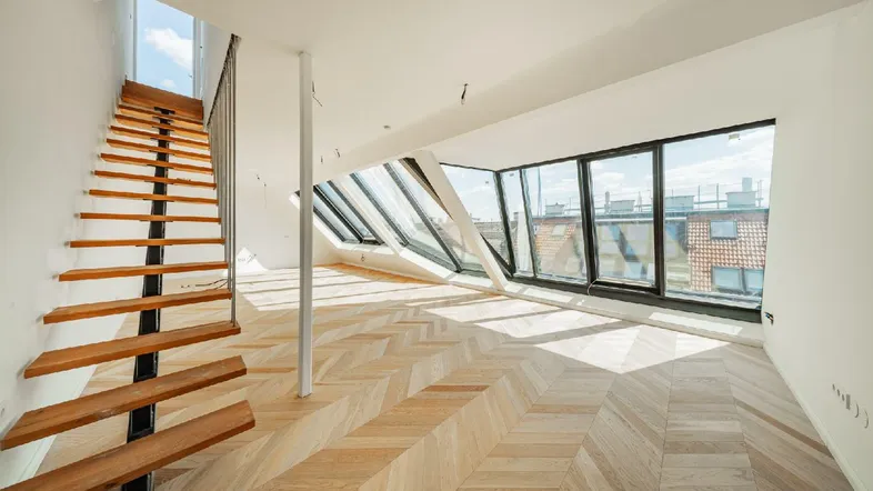 Heller Wohnbereich mit Fischgrätparkett, großen Dachfenstern und moderner Treppe.