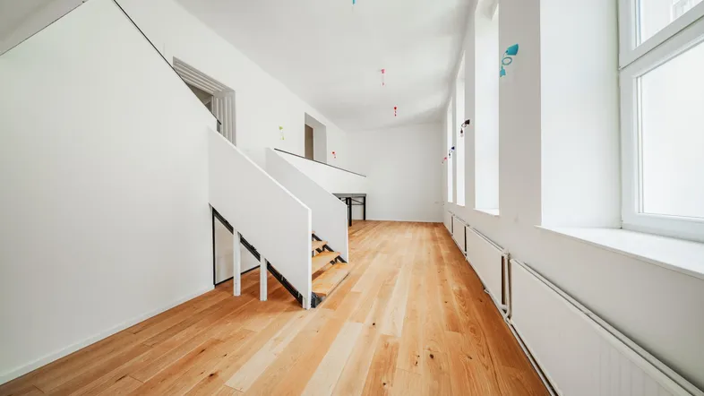Langer, heller Raum mit Holzboden und Treppe, viele Fenster sorgen für eine freundliche Atmosphäre.
