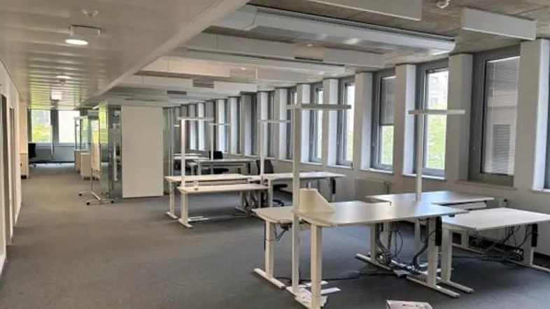 Geräumiges Großraumbüro mit modernen Schreibtischen, Teppichboden und großen Fenstern für viel Tageslicht.