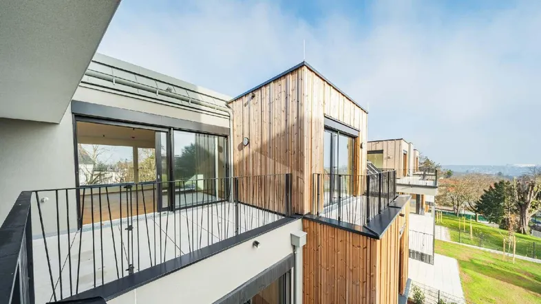 Moderne Architektur mit Holzfassade und mehreren Balkonen, die einen weiten Blick ins Grüne bieten.