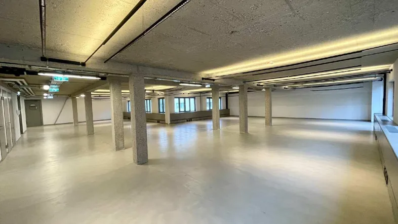 Großer, offener Büroraum mit Sichtbetondecke, Säulen und modernen Lichtleisten.