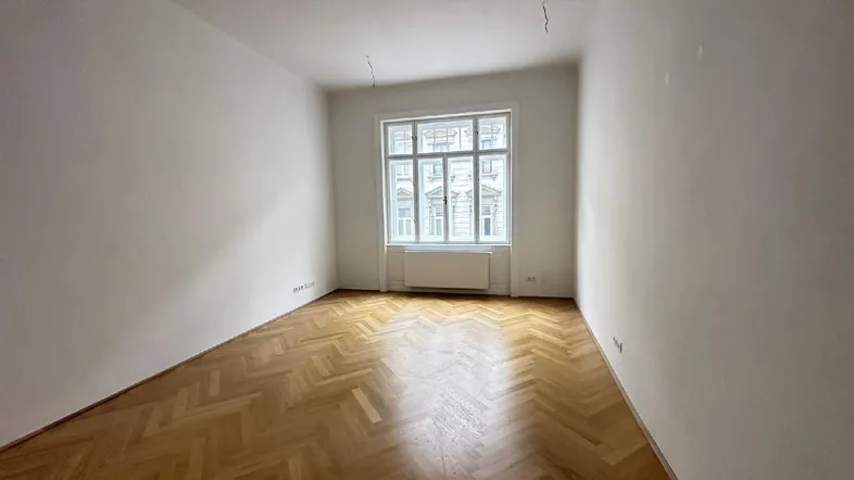 Helles, leeres Zimmer mit Fischgrätparkett und großem Fenster, bereit zur individuellen Gestaltung.