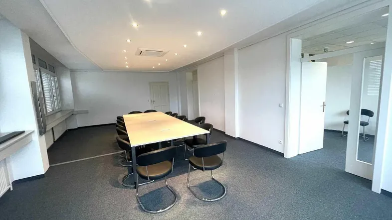 Geräumiger Konferenzraum mit großem Tisch, bequemen Stühlen und Teppichboden, ideal für Besprechungen.