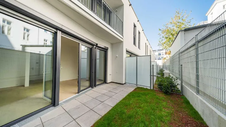 Moderne Terrasse mit direktem Zugang zum kleinen Gartenbereich, umgeben von einer Metallzaun.