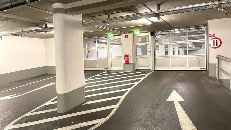 Tiefgarage mit markierten Parkplätzen, Säulen und Zugang zu den Ausgängen und einer Rampe.