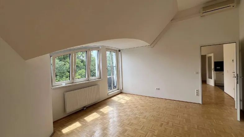 Helles Zimmer mit Parkettboden, Dachschrägen und Zugang zu einem kleinen Balkon.