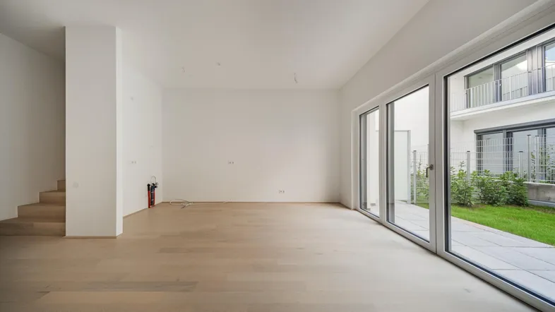 Helles, leeres Wohnzimmer mit Holzboden und großen Schiebetüren zum Gartenbereich.