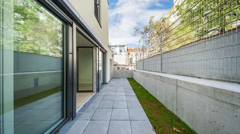 Gepflasterte Terrasse mit Zugang zu den Innenräumen und einer kleinen Rasenfläche.