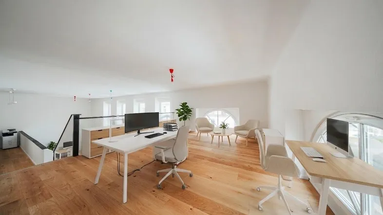 Helles, offenes Büro mit Holzboden, modernen Arbeitsplätzen und gemütlicher Sitzecke unter Rundfenstern im Dachgeschoss.