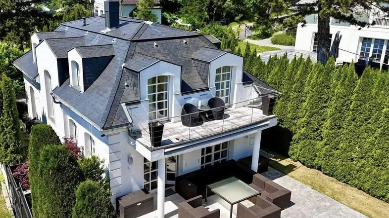 Elegante Stadtvilla mit großzügiger Terrasse, Balkon und gepflegter Hecke im Grünen.