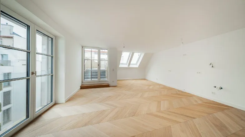 Helles Zimmer mit Fischgrätparkett, großen Fenstern und Dachschrägen, bereit zum Einzug.