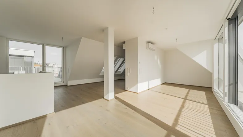Helles, offenes Wohnzimmer mit Holzboden, großen Fenstern und Zugang zu einem Balkon.