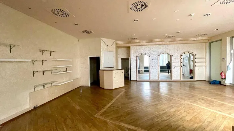 Großer Verkaufsraum mit Holzboden, Wandregalen, Spiegeln und Deckenlüftung in einem Geschäftshaus.