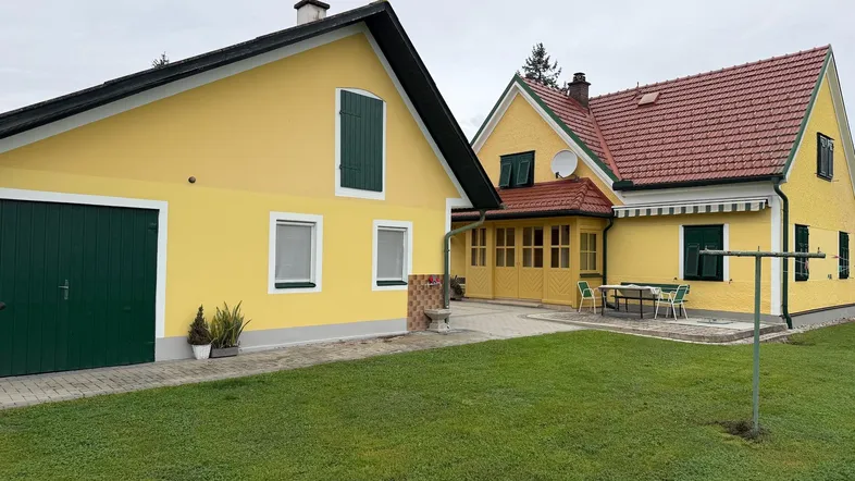 Ansicht des Hauses mit gelber Fassade, grünem Garten und einer kleinen Terrasse mit Sitzgelegenheiten.
