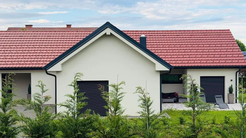 Modernes Einfamilienhaus mit rotem Ziegeldach, weißer Fassade und gepflegtem Vorgarten.