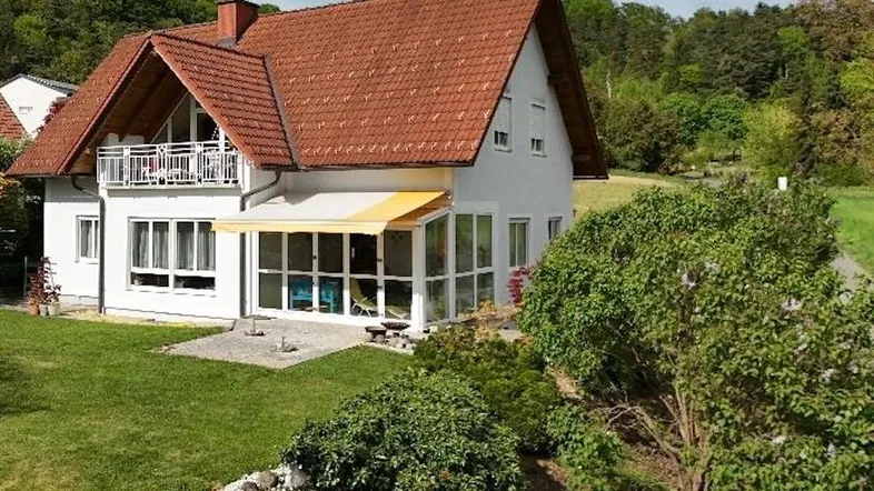 Attraktives Haus mit Balkon, Wintergarten und weitläufigem Rasen in grüner Umgebung.
