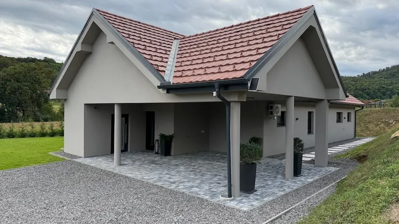 Modernes Einfamilienhaus mit Carport und gepflastertem Vorplatz unter bewölktem Himmel in ländlicher Umgebung.