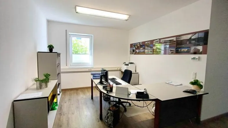 Geräumiges Büro mit modernem Schreibtisch, Holzfußboden und Blick ins Grüne durch das Fenster.