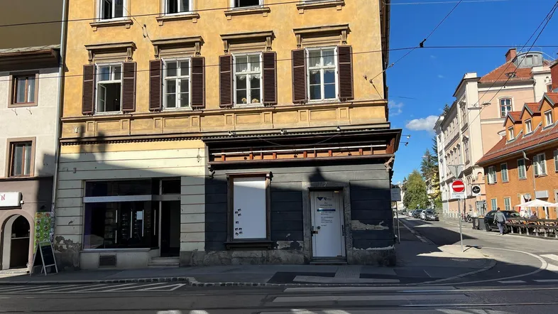 Gelbes Mehrfamilienhaus mit Geschäften im Erdgeschoss und Blick auf die belebte Straße.