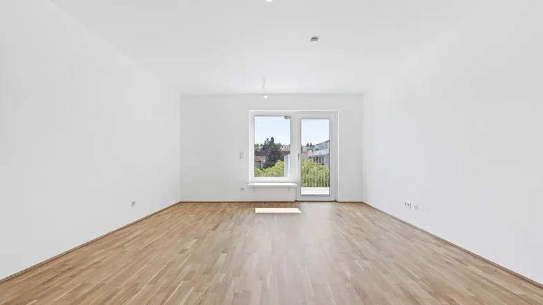 Helles, leeres Zimmer mit Parkettboden und Zugang zu einem Balkon, ideal als Wohnbereich.