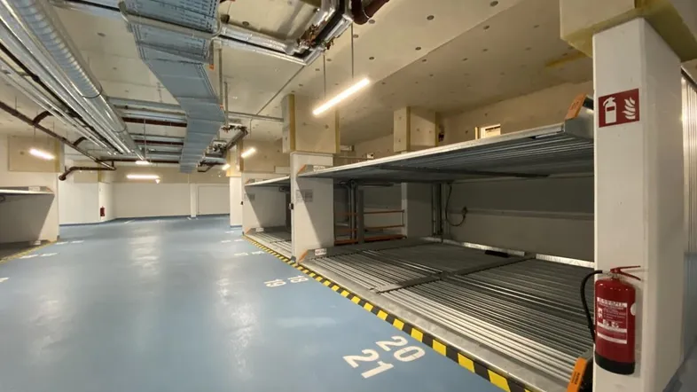 Tiefgarage mit mechanischen Parksystemen, blauer Boden und sichtbaren Installationen an der Decke.
