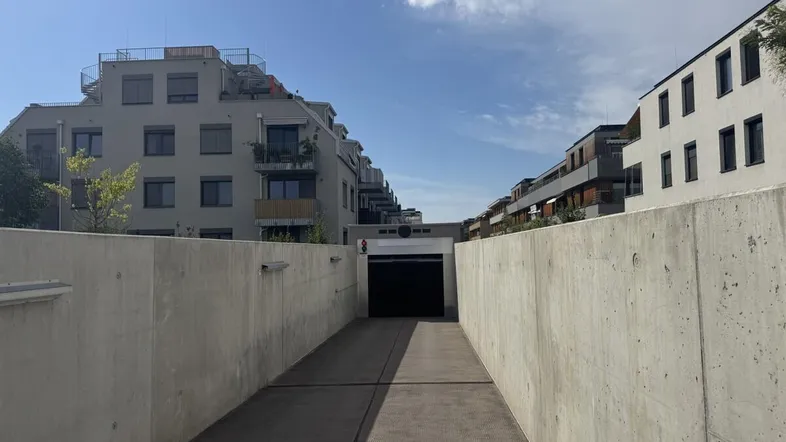 Einfahrt zur Tiefgarage mit modernen Wohngebäuden im Hintergrund unter blauem Himmel.