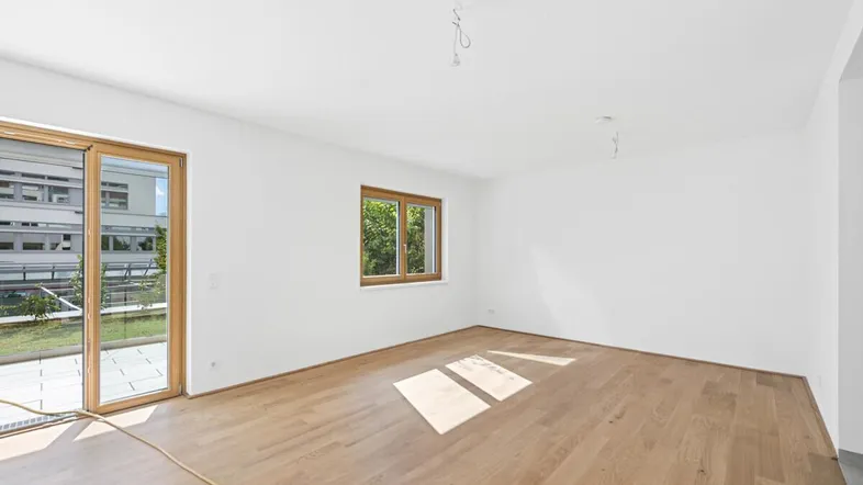 Helles, leeres Zimmer mit Holzboden und Zugang zu einem Balkon, ideal für ein Wohnzimmer.