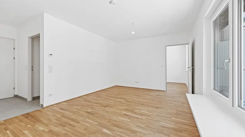 Helles, leeres Zimmer mit Parkettboden und weißen Wänden, bereit zur individuellen Gestaltung.