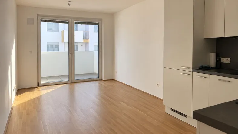 Heller offener Wohnbereich mit integrierter Küche, Parkettboden und Zugang zu einem Balkon.
