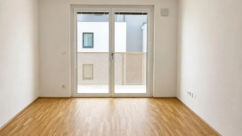 Helles Zimmer mit Parkettboden und Zugang zu einem Balkon, ideal als Wohn- oder Schlafbereich.