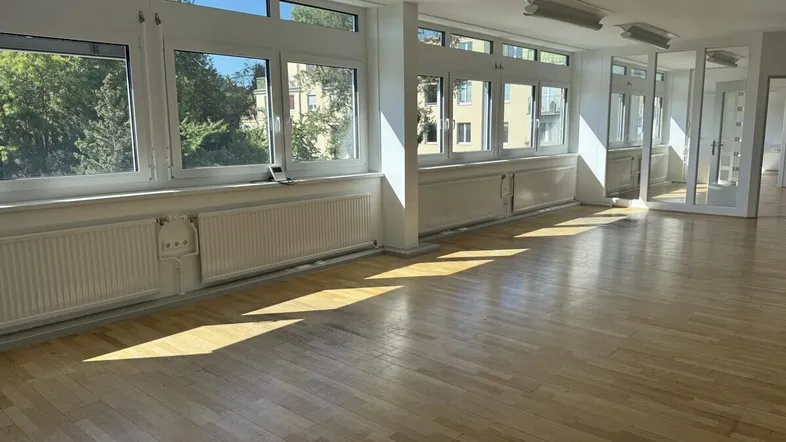 Helles, leeres Büro mit großen Fenstern, die viel Tageslicht hereinlassen und einen Blick ins Grüne bieten.