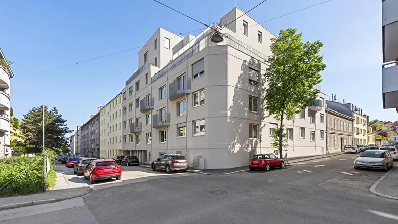 Modernes Eckgebäude mit mehreren Balkonen und großen Fenstern in einer städtischen Umgebung.