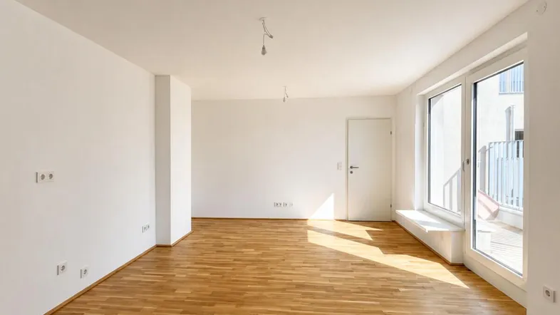 Helles, leeres Zimmer mit Parkettboden und Zugang zu einem Balkon, ideal für Wohn- oder Schlafbereich.