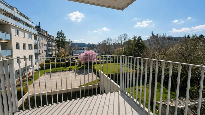 Geräumiger Balkon mit Fliesenboden und Blick auf die grüne Umgebung und andere Gebäude.