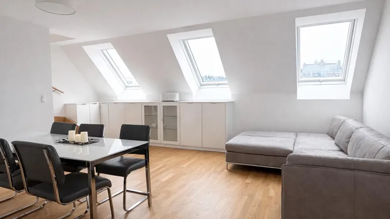 Helles Dachgeschoss-Wohnzimmer mit Essbereich, Parkettboden und mehreren Dachfenstern.