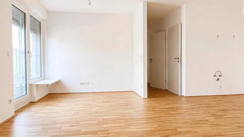 Heller, leerer Raum mit Parkettboden und Zugang zu einem Balkon, bereit zur Einrichtung.