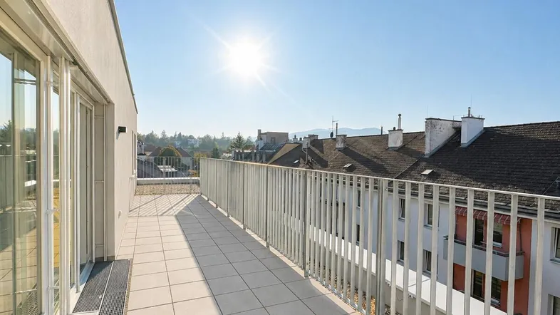 Sonnige Terrasse mit Fliesenboden und modernem Geländer bietet weiten Stadtblick.