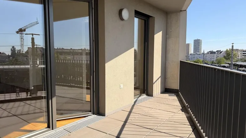 Heller Balkon mit Fliesenboden und Blick auf die Stadt sowie eine Baustelle im Hintergrund.