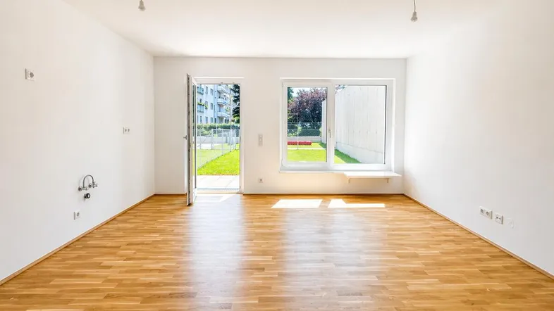 Heller, leerer Raum mit Holzboden und direktem Zugang zu einem kleinen Gartenbereich.