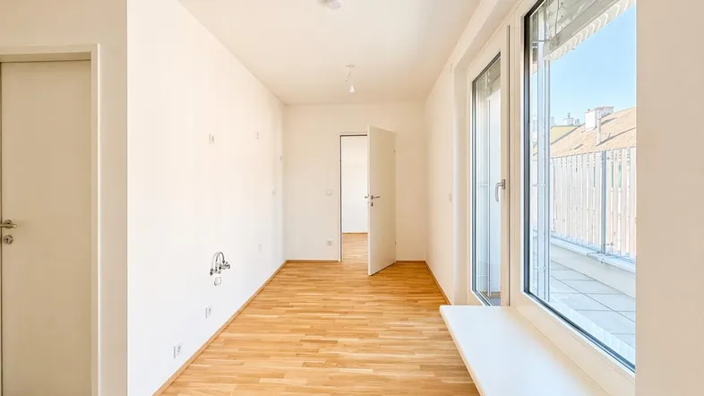 Helles, leeres Zimmer mit Parkettboden und Zugang zu einem Balkon oder einer Terrasse.