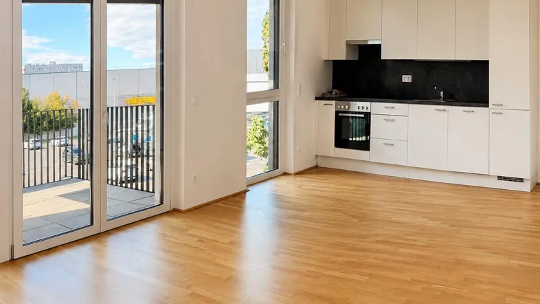 Heller Wohn- und Essbereich mit integrierter Küche, Parkettboden und Zugang zu einem Balkon.