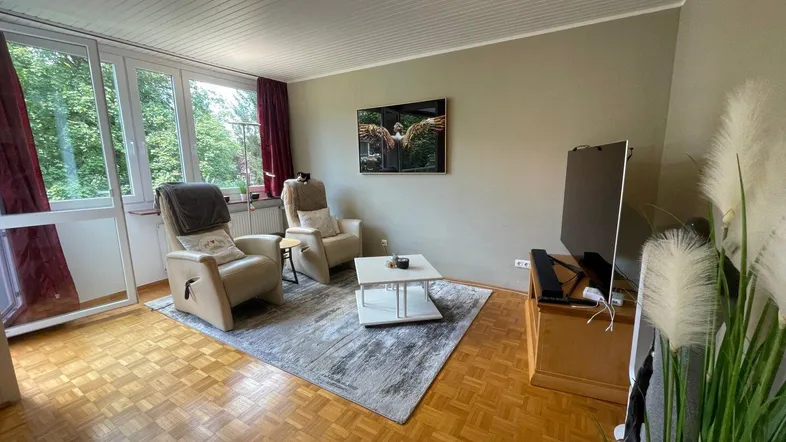 Gemütliches Wohnzimmer mit Parkettboden, bequemen Sesseln und Zugang zum Balkon.